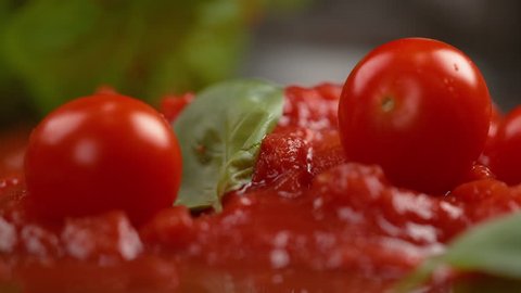 SLOW MOTION, MACRO, DOF: Small tomatoes fall into the fresh vegetarian tomato sauce with basil. Delicious marinara splatters across the table as cherry tomatoes are dropped into the cooked sauce.