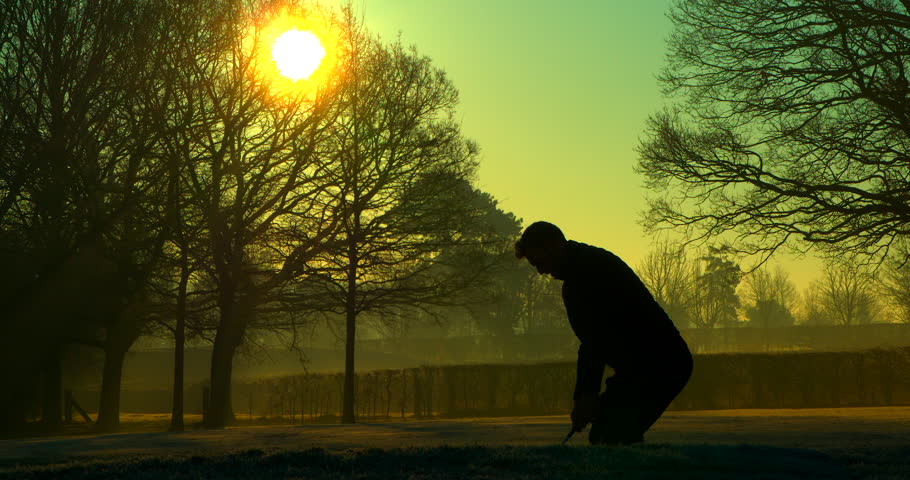 A Golfer chips out of a sand trap at sunrise.
