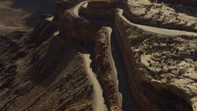 Aerial flyover view of car driving on winding road in canyon landscape / Mexican Hat, Utah, United States