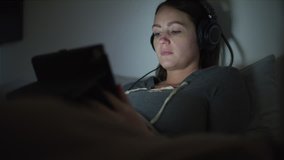 Woman in bed watching movie on digital tablet at night / Murray, Utah, United States