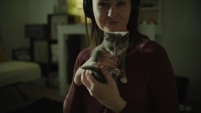 Portrait of smiling woman holding cat and listening to headphones / Murray, Utah, United States