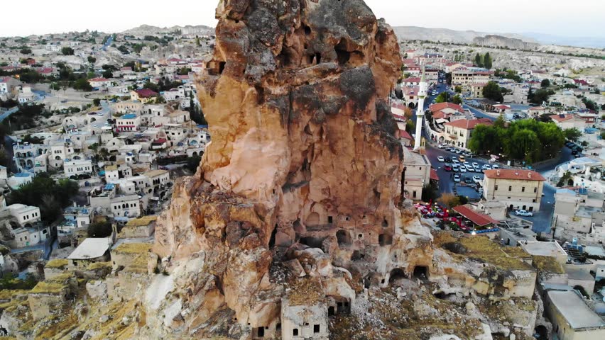 Flying over Ortahisar Castle in Cappadocia in Urgup. Cave hotels and buildings behind giant fairy chimney in tourist town in Turkey. Spire rising above small village in remote Kapadokya.