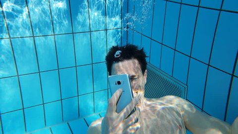 A man texting and taking photos with a phone under water in a swimming pool