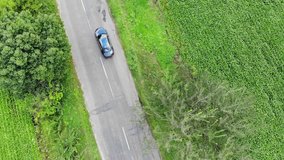 Aerial shot stock video footage camera haunts the car that drives along the road between the green fields. 4k video. Top view