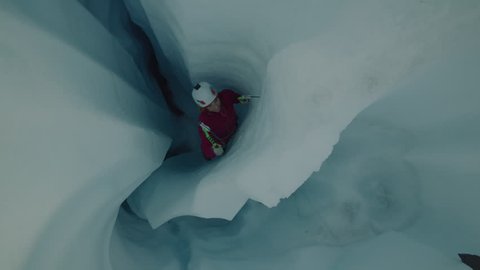 High angle view of ice climber ascending narrow crevice on glacier using hooks / Palmer, Alaska, United States