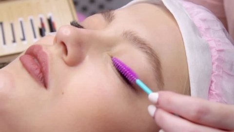 Eyelash Extension Procedure. Woman Eye with Long false Eyelashes. Closeup macro shot of fashion eyes in beauty salon. Hands beautician. Eyelash wizard brushes client's eyelashes with a brush
