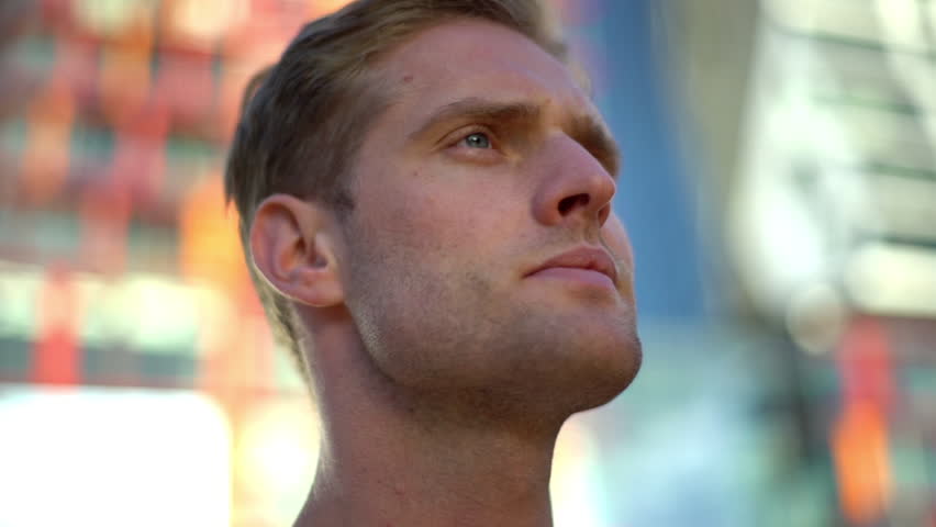 Slow-motion low-angle portrait handsome blond caucasian man with blue eyes touching bristle jawline, looking aside frowning thoughtful, thinking, making decision outside, exploring city landscapes