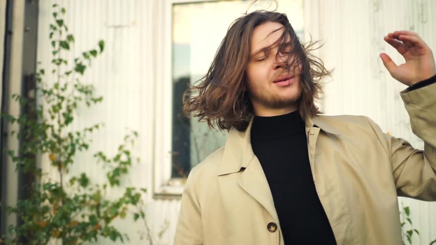 The man adjusts his long hair. A man adjusts his clothes. A handsome man posing in front of the camera. A man in a coat and sunglasses.Fashion 90