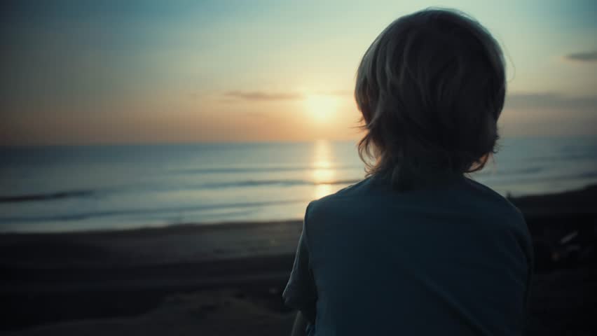 Child admiring beautiful sunset on shore. Looking at ocean view, thinking about life, dreaming. Happy childhood. Enjoying afternoon peace and nature. Quiet, calm mood. Vacation travel | Shutterstock HD Video #1024489139