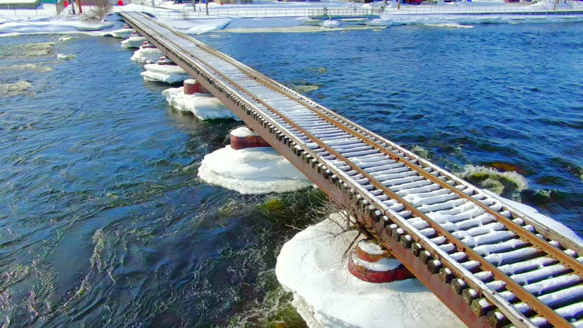 Scenic snow covered railroad trestle bridge over icy river.
