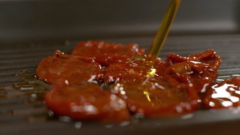 SLOW MOTION, MACRO, DOF: Organic olive oil splashes over the homegrown sundried tomatoes heating up on the teflon grill pan. Delicious cured cherry tomatoes are enriched by pouring olive oil over them