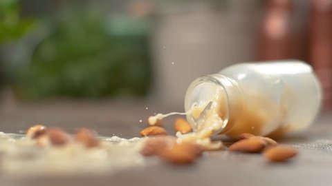 SLOW MOTION, MACRO, DOF: Refreshing almond milk spills over the raw organic almonds after a glass bottle falls onto the kitchen counter. Light brown liquid splashes over scattered unpeeled almonds.