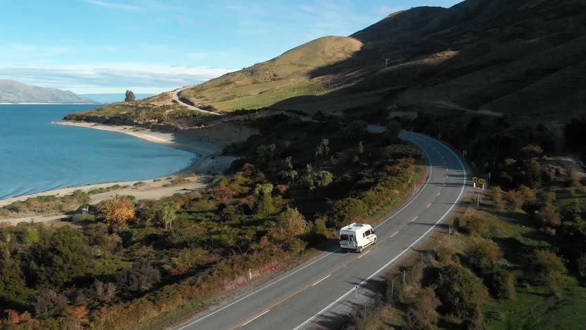 Slowmo Aerial Drone following a campervan with a view of beautiful blue Lake Hawea, field of sheep and mountains in late afternoon in New Zealand Royalty-Free Stock Footage #1024496819