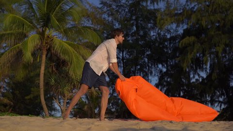Slowmotion shot of A Young Man Inflates An Inflatable Sofa on a beautiful beach