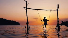 Girl in vacation holidays at the beach relaxing on a rope swing above sea water at sunset in tropical resort, warm summer outdoor leisure activity, inspiring lifestyle video