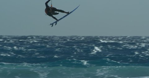 A Kitesurfer riding his word strapless flying through the air and maintaining the grab.