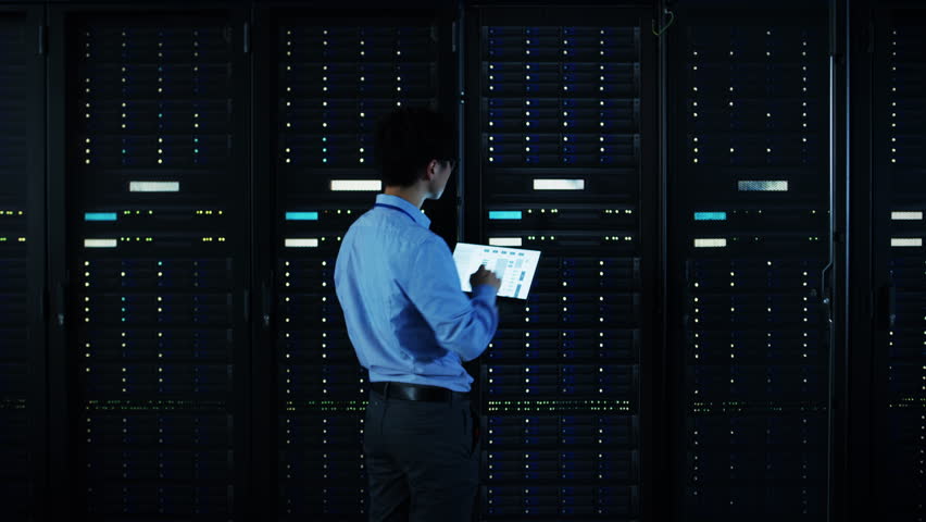 The Concept of Digitalization of Information: IT Specialist Standing In front of Server Racks with Laptop, He Activates Data Center with a Touch Gesture. Animated Visualization of Network Data Royalty-Free Stock Footage #1024515128