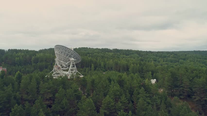 Aerial view shot of radio telescope in observatory. Backward flying. Move back. Green summer forest. Cloudy. Royalty-Free Stock Footage #1024516130