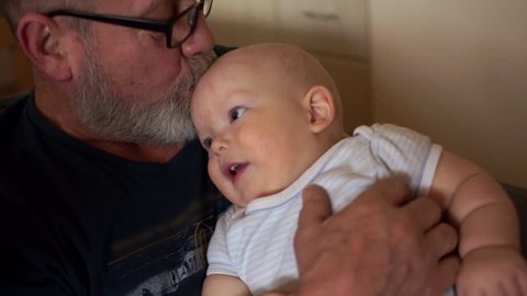 Grandfather is holding a little grandson. An elderly man with a gray beard and a little one year old boy