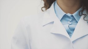 Beautiful young brunette doctor wearing medical clothes on gray background. During this she puts the phonendoscope on her neck. Has beautiful black long hair. Dressed in glasses Slow video.