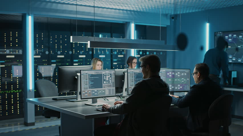 Team of IT Programers Working on Desktop Computers in Data Center Control Room. Young Professionals Writing on Sophisticated Programming Code Language. Elevated Moving Camera Shot Royalty-Free Stock Footage #1024519529