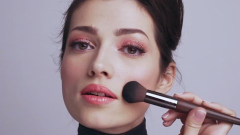 Woman makes makeup. Young woman makes  blush on the face  using makeup brush. Cosmetic concept. Slow motion footage. 