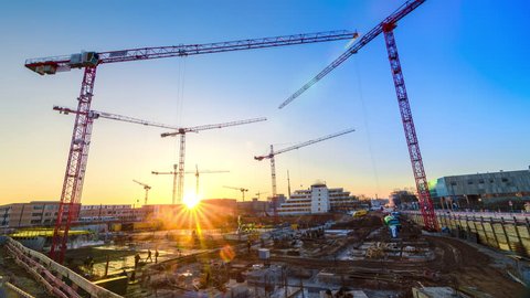 Timelapse footage of a large construction site with several busy cranes at dusk, with clear blue sky and the setting sun