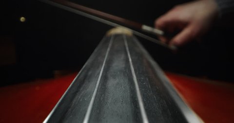 Slow motion artistic macro of master artisan luthier playing with a bow on a handmade violin or cello. Shot in 8K. Concept of spiritual instrument, art, orchestra, passion for music, sound, precision