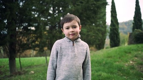 Portrait of a young boy standing in a green yard in rural Tuscany. Wide to medium shot on 8k helium RED camera.