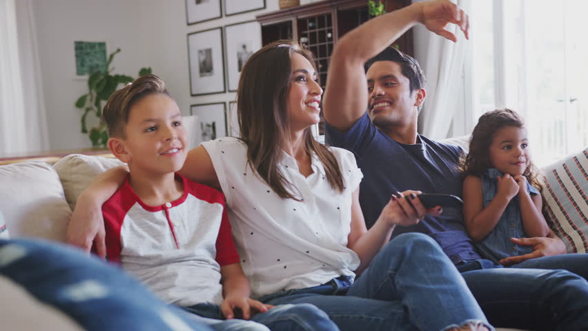 Young Hispanic family sitting on the sofa at home watching TV together, close up