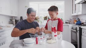 Jump cut clip of father and pre-teen son preparing cake mix and baking cakes in their kitchen