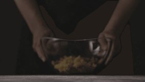 Female's hands moving toward big glass bowl with falling colorful italian pasta Rotini on a dark wooden background on a black. Slow motion, Full HD video, 240fps, 1080p.