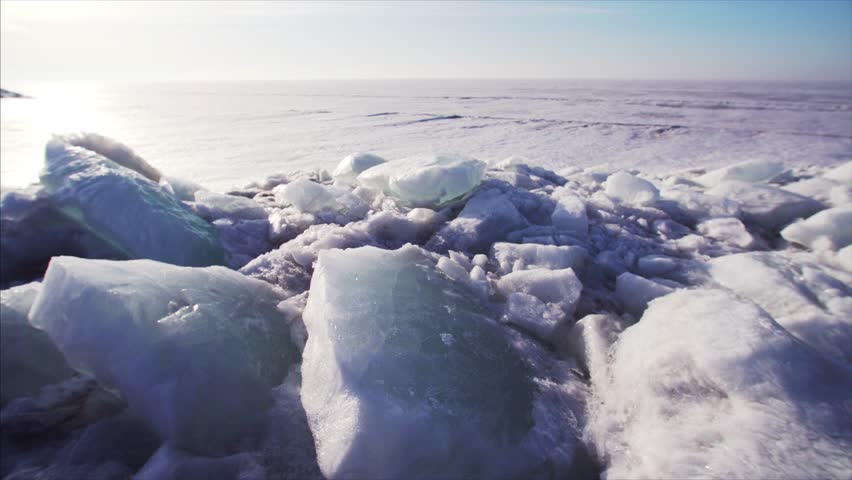 Sliding view of big frozen lake and huge white ice blocks on the foreground. Sunny winter day
