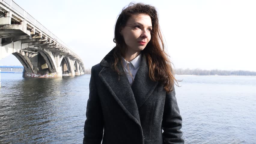 Young brunette girl shoots with a gun near the river in the city
