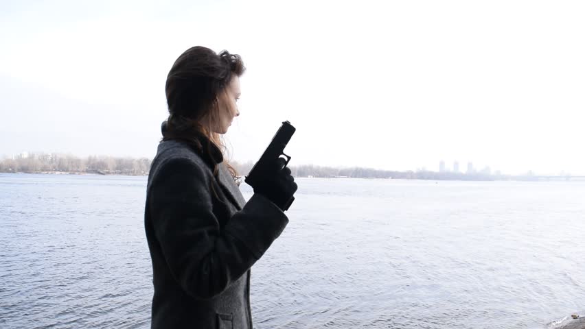 Portrait of a young brunette girl with a gun near the river
