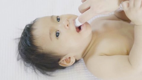 Mother use finger to clean mouth asian baby tongue with clean gauze.Selective focus
