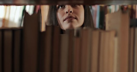 Female university student searching for book on bookshelves in library