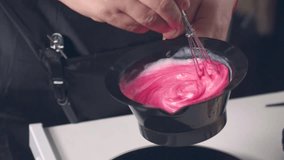 A woman mixes red and white hair dye in a black jar, turns pink paint. Slow Motion Video