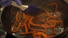 We can see the cooking process on the video. Vegetables are frying on pan. Chef in cooking gloves mix them with a spoon.