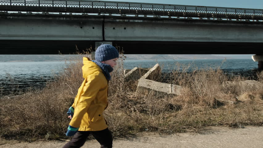 The child in yellow jacket runs near the bridge. 
