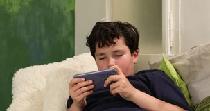 Portrait of a preteen boy with smartphone sitting on sofa at home. Kid watching to screen, reading, typing, playing games. Technology, internet communication and people concept, Smartphone addiction