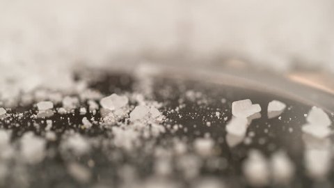 SLOW MOTION, DOF, MACRO: White crystals of sugar bouncing off the hard black surface of the kitchen table. Coarse crystals of rock salt are scattered across the granite countertop of a chef's table.