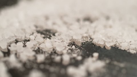SLOW MOTION, MACRO, DOF: Pristine white salt crystals are sprinkled across the black surface of the chef's table. Cool shot of sugar crystals fall and bounce around the granite kitchen countertop.