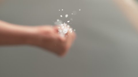 SLOW MOTION, MACRO, BOTTOM UP, DOF: Unrecognizable chef sprinkles white sugar crystals over the camera. Caucasian person crushing sea salt with their hand and scattering it across the kitchen floor.