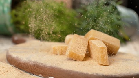 SLOW MOTION, MACRO, DOF: Parmesan flakes fall on the cheese cubes on the wooden board. Mouth-watering shot of parmesan cheese being grated over the whole cheese cubes. Gourmet delicacy from Italy.