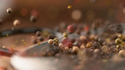 MACRO, DOF, SLOW MOTION: Fragrant colorful peppercorns bounce out of the metal frying pan after falling onto the table. Cool shot of pepper flakes and whole peppercorns falling along with a pan.