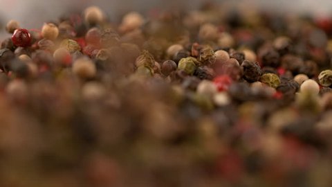 SLOW MOTION, MACRO, DOF: Aromatic pepper mix is toasting and swirling in a moving frying pan. Colorful peppercorns are being mixed and roasted in a hot pan. Flavorful and aromatic spices roasting.