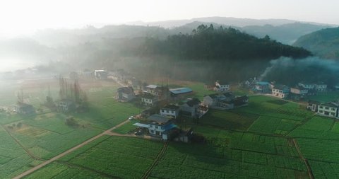 Aerial View: beautiful countryside landscape in the early spring morning of village, fields at the bottom of a mountain in mist at dawn, car parking on the country road, in Sichuan China,4K Drone clip
