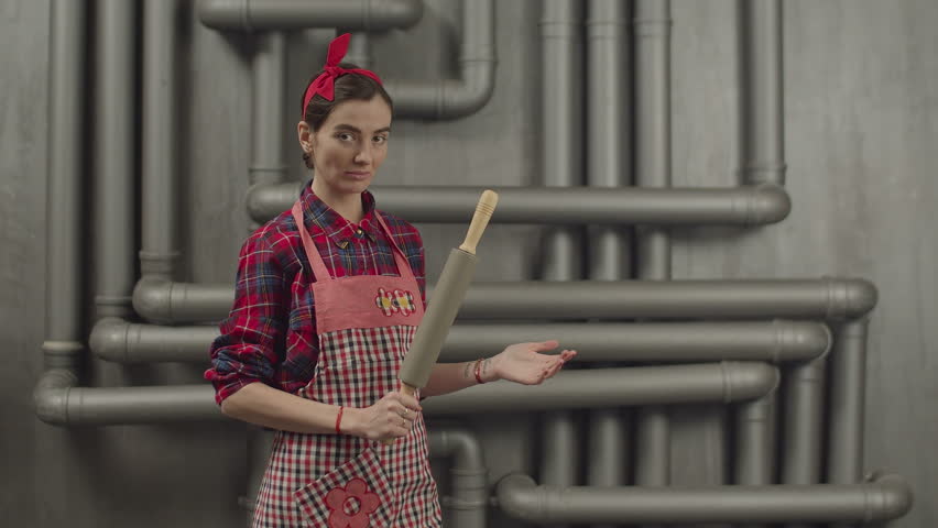 Serious determined housewife in apron and headband with rolling pin clapping on hand with angry and irritated expression. Confident attractive woman with rolling pin looking threatening and frustrated Royalty-Free Stock Footage #1024613873