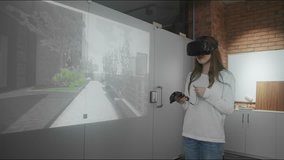 A young girl client studies the design project in virtual reality glasses, looks around, controls the joystick. The future of architecture and construction industry. Modern loft office. Red epic. 4K